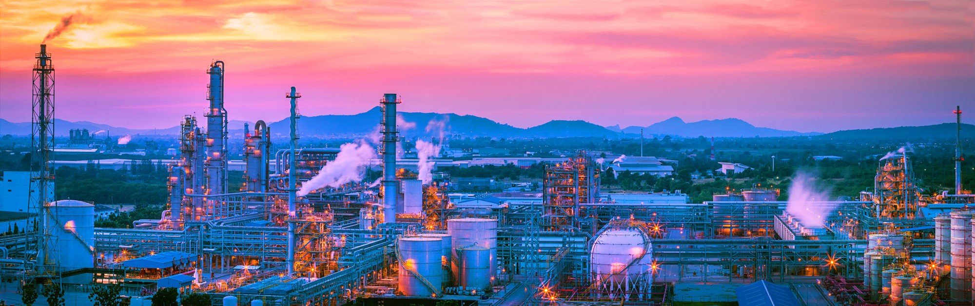 Industrial refinery with illuminated pipework and processing towers at dusk